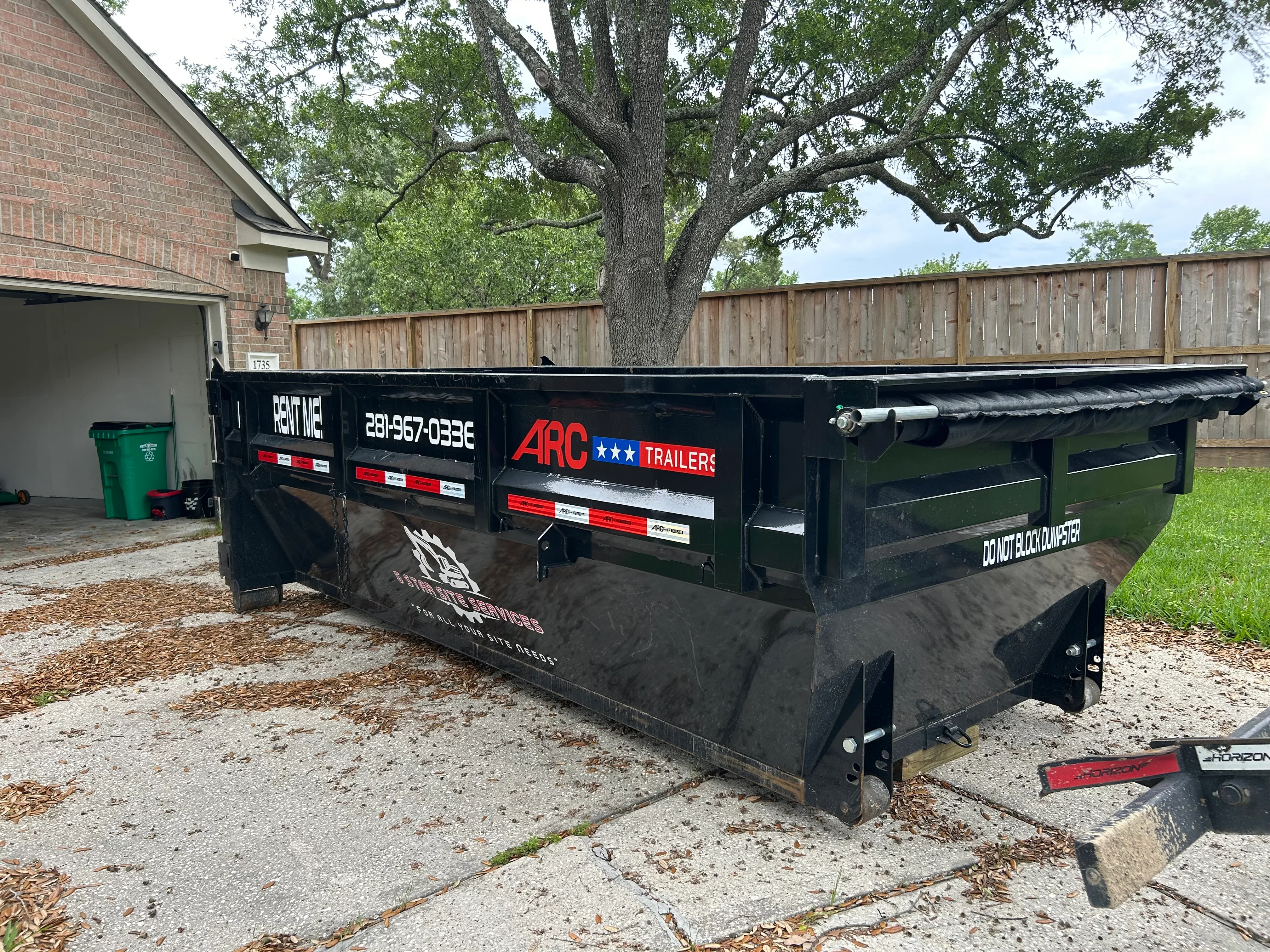 Black flatbed trailer with custom vinyl wrap, red safety reflectors, and company branding