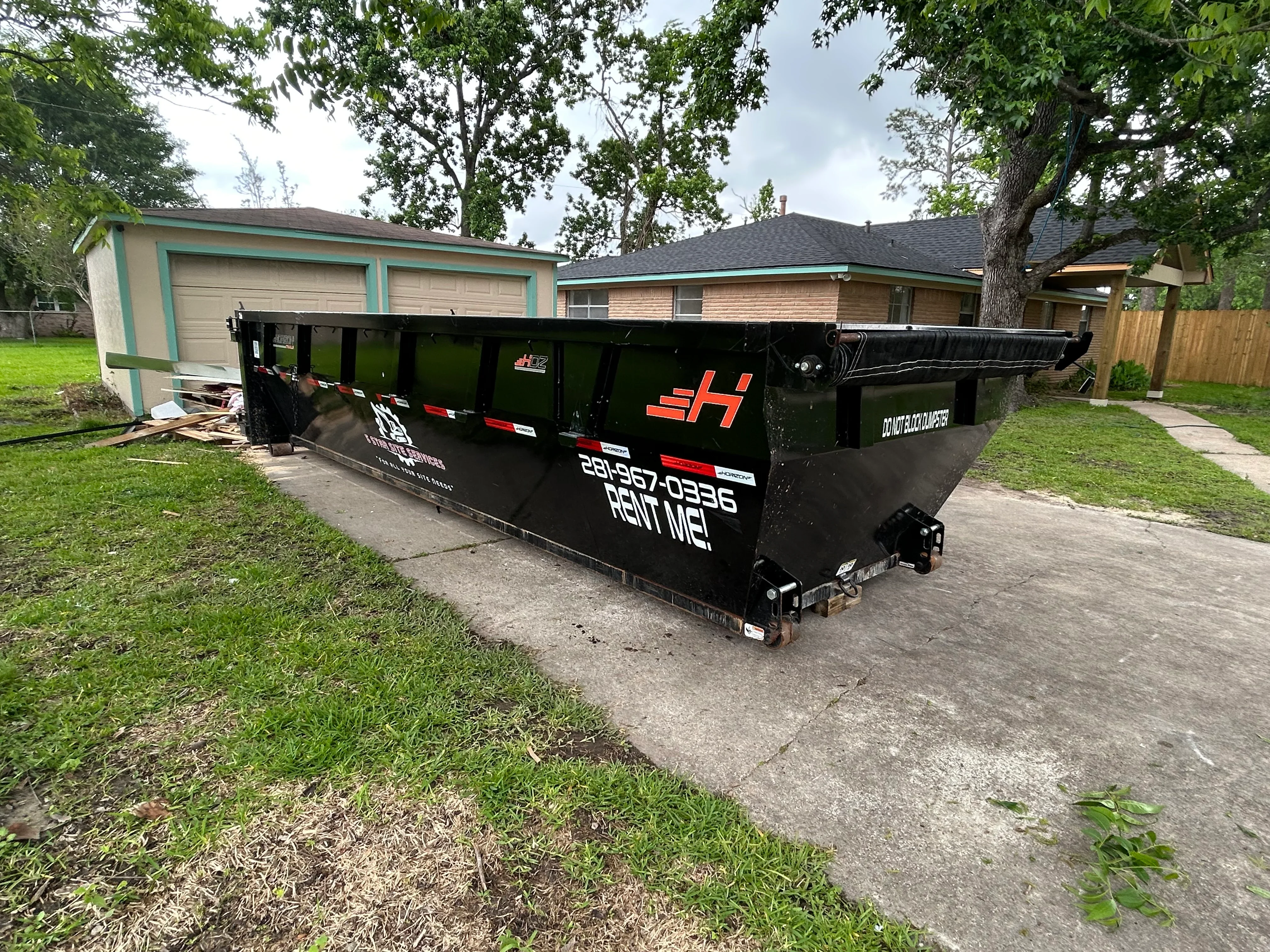 Black open-top dumpster with hydraulic lift system in residential driveway