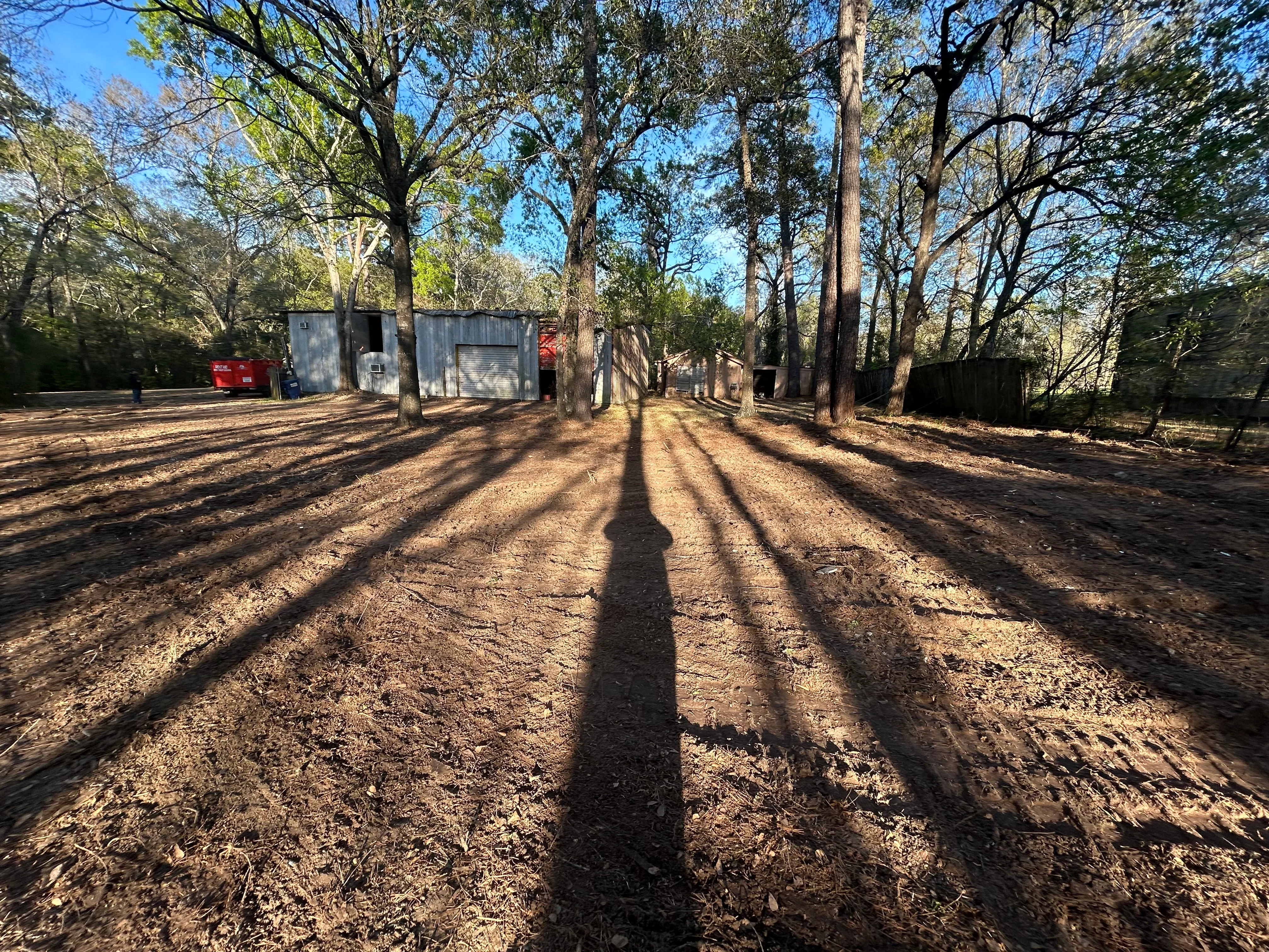 Cleared dirt lot with mature trees, metal structures, and organized site layout