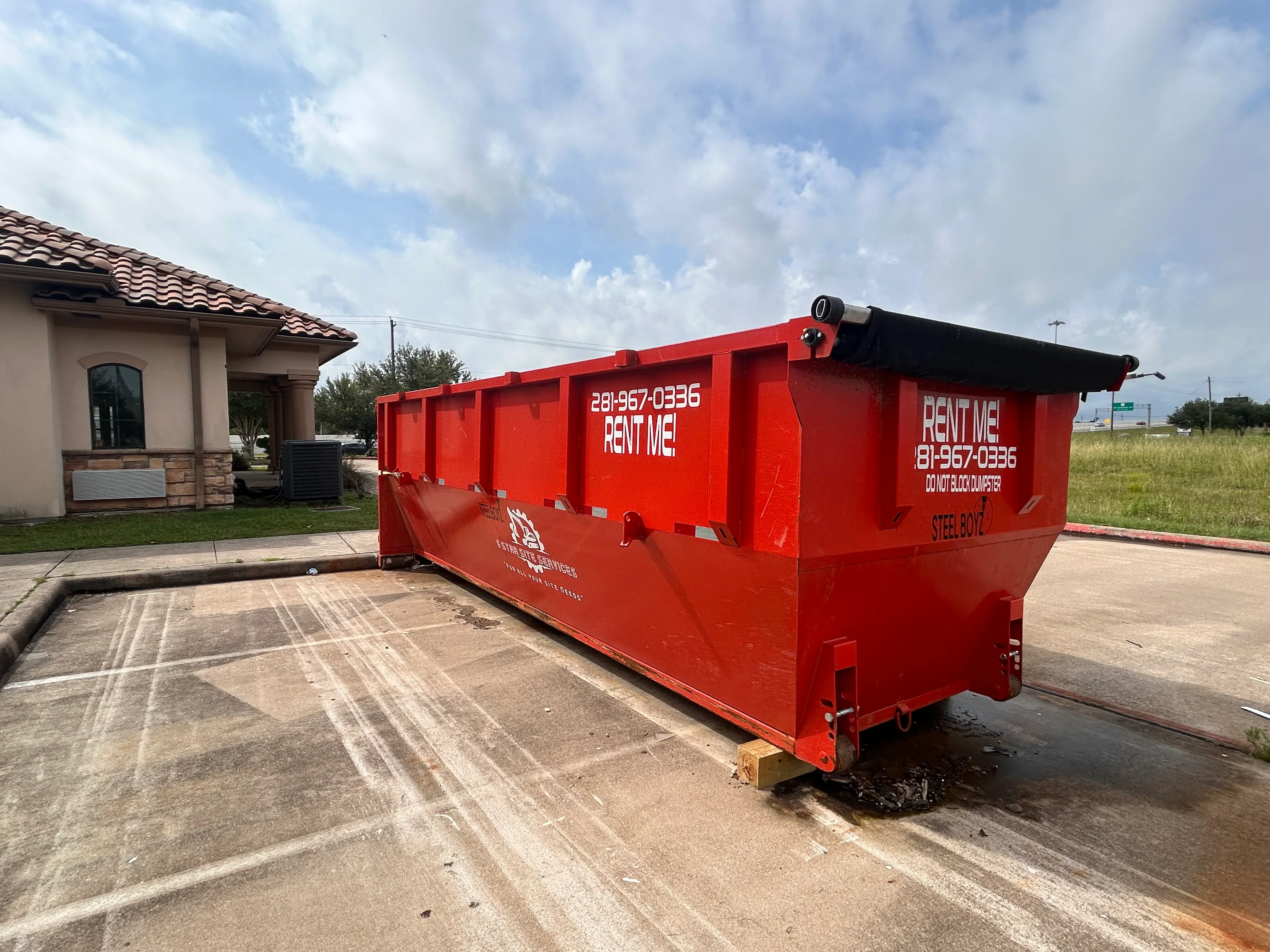 Red steel roll-off dumpster with hinged cover on residential driveway