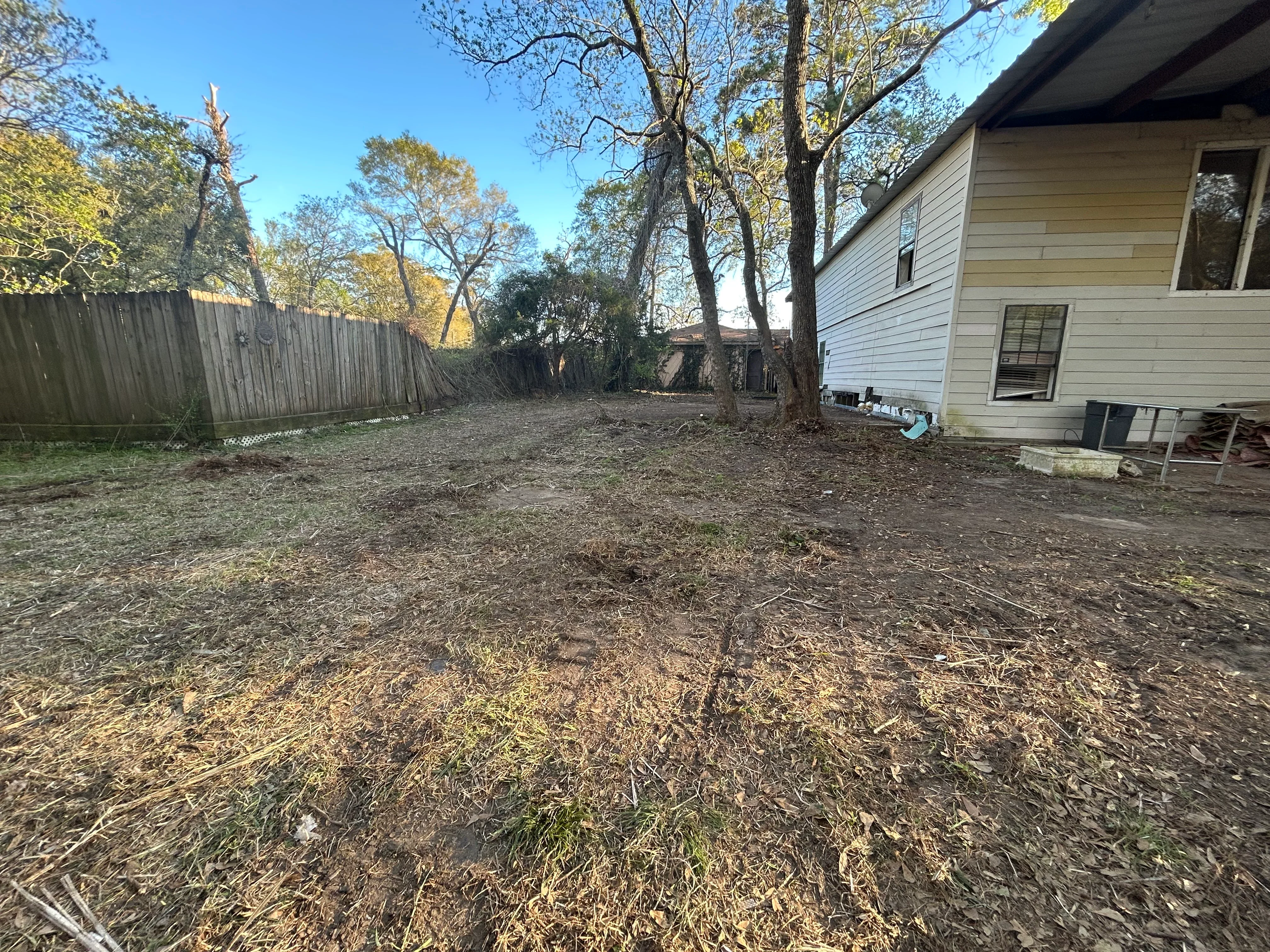 Cleared residential backyard with bare earth, wooden fence, and mature trees