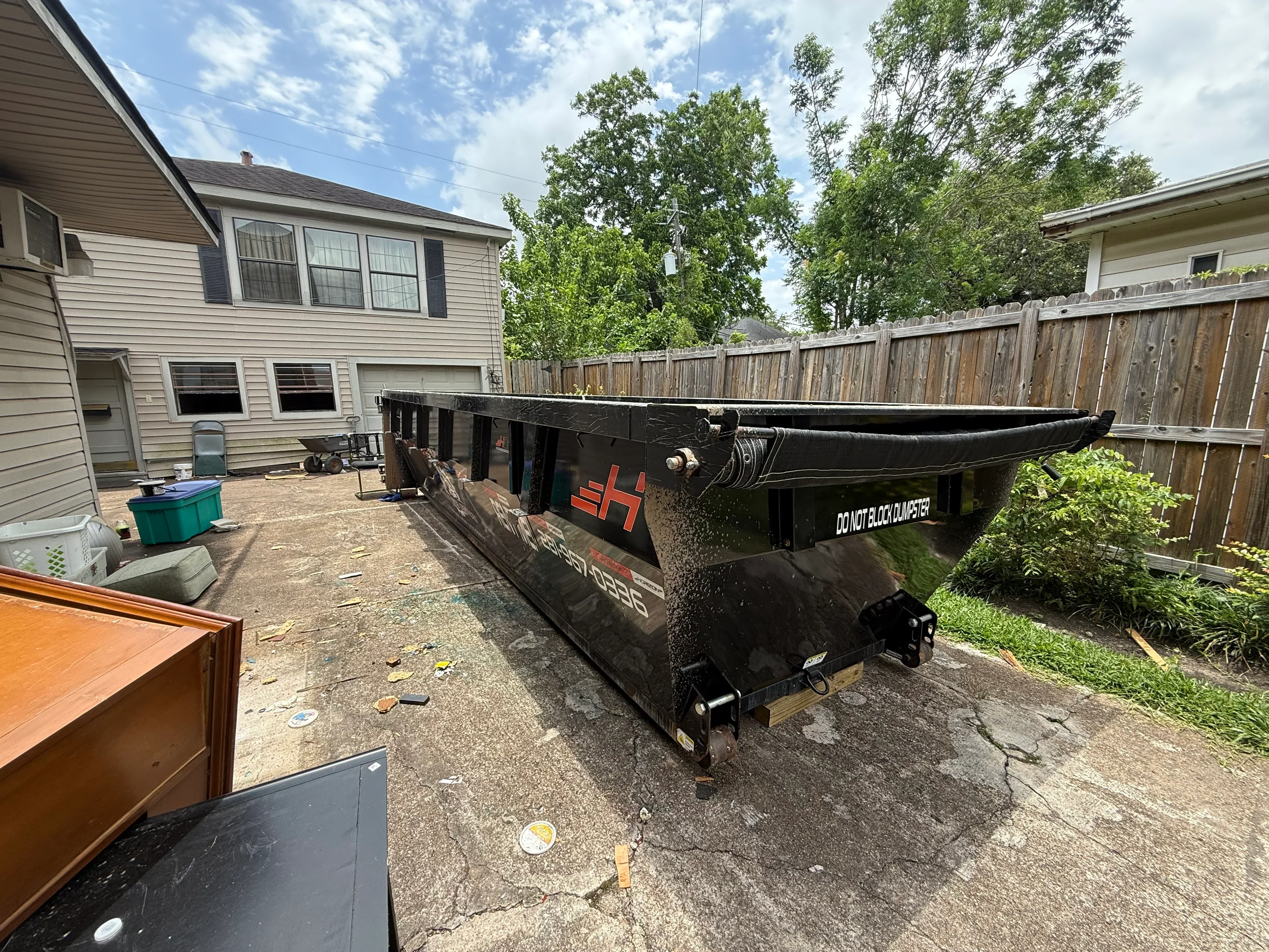 Black roll-off dumpster with hydraulic system in residential backyard setting