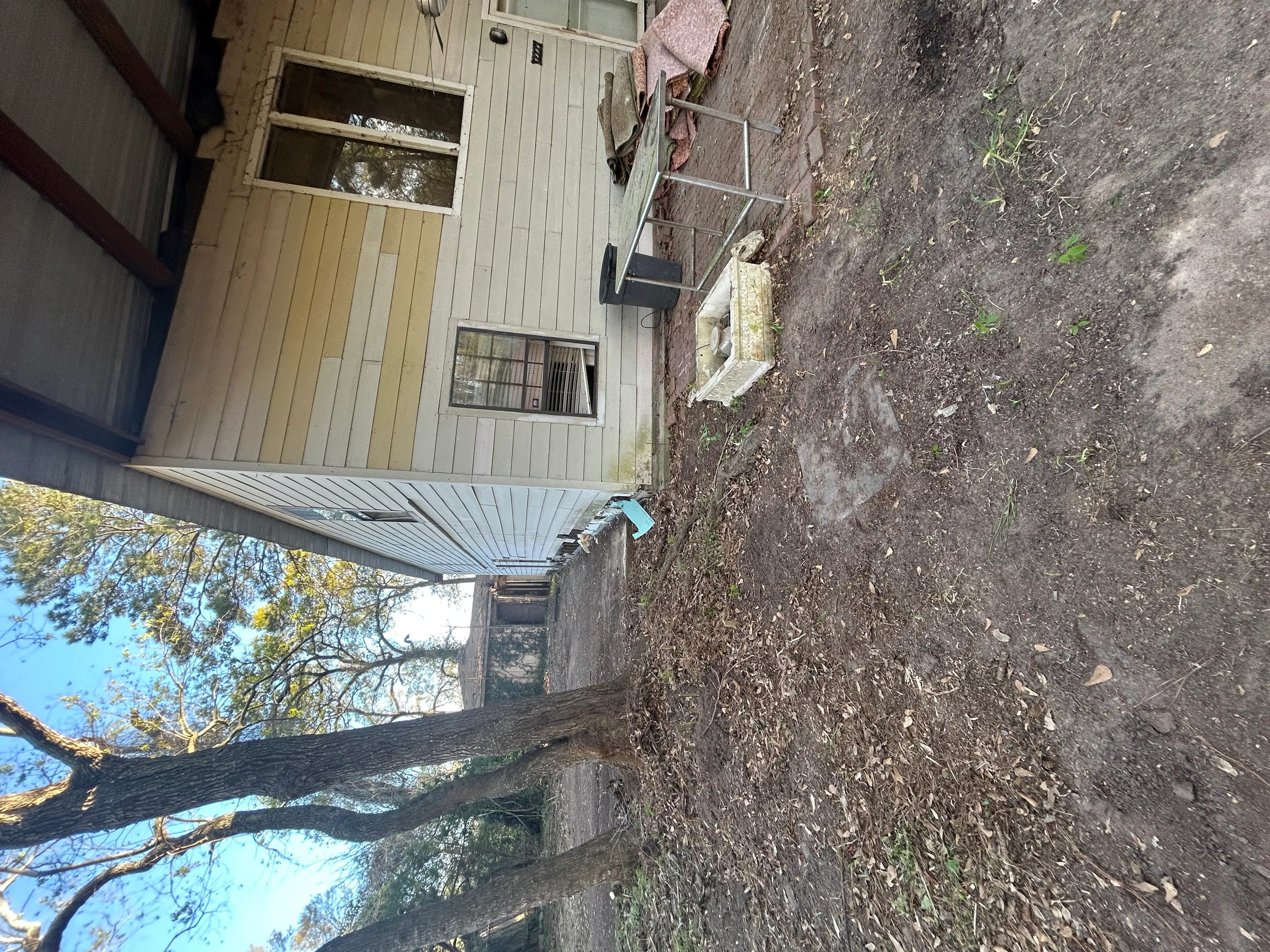 Cleared residential lot with removed debris and exposed soil, metal roofed structure visible
